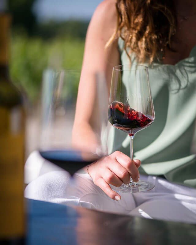 A woman with long hair, holding a glass of red wine, seated at a table.