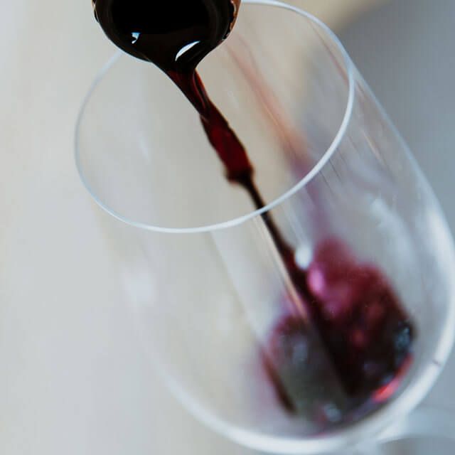 A hand pouring rich red wine into a clear glass, capturing the moment of service.